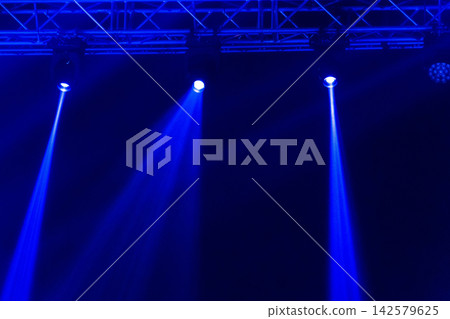 Blue stage spotlights shining from overhead truss in dark venue Blue stage spotlights shining from overhead truss in dark venue 142579625