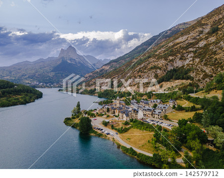 Pyrenees Village and Twin Peaks of Foratata. Aerial view of a Pyrenees village beside the turquoise Lanuza reservoir with the twin summits of Pena Foratata behind near Formigal, Spain, a scenic mounta Pyrenees Village and Twin Peaks of Foratata. Aerial view of a Pyrenees village beside the turquoise Lanuza reservoir with the twin summits of Pena Foratata behind near Formigal, Spain, a scenic mounta 142579712