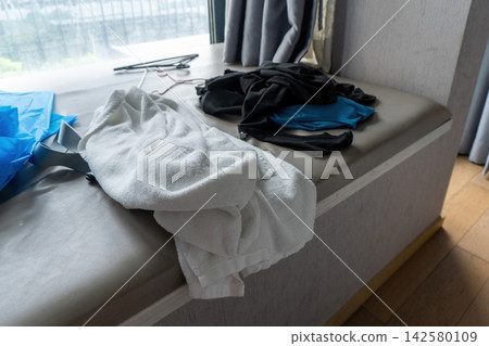 Folded towels and clothes on bench by window 142580109