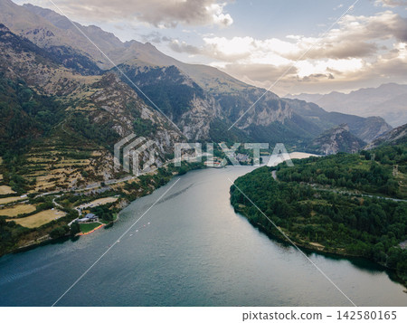 Reservoir Bending Through the Green Pyrenees at Dusk. Aerial view of the Lanuza reservoir bending through the green mountains of the Spanish Pyrenees near Formigal, Spain, a serene and moody landscape Reservoir Bending Through the Green Pyrenees at Dusk. Aerial view of the Lanuza reservoir bending through the green mountains of the Spanish Pyrenees near Formigal, Spain, a serene and moody landscape 142580165