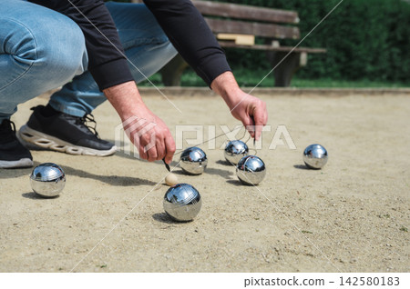 Man measuring with string which boule is closest to jack. Man bent down measuring with string tool which steel boule is closest to wooden jack on gravel court, precise scoring moment during outdoor pe 142580183