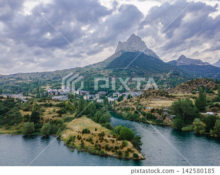 Mountain Village and Reservoir Below Foratata Peak. Aerial view of a mountain village and the turquoise reservoir with the Pena Foratata peak beyond in the Spanish Pyrenees, Aragon, a scenic and majes 142580185