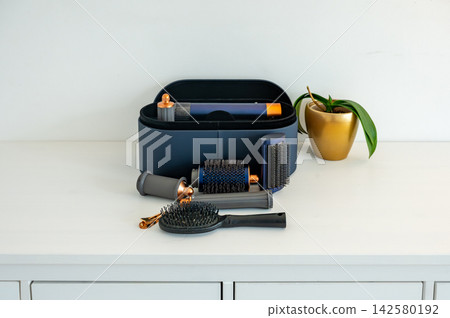 Round brush and paddle brush crossed beside styling case. Round barrel brush and paddle brush arranged in crossed composition beside open styling case, hair care tools still life for beauty Round brush and paddle brush crossed beside styling case. Round barrel brush and paddle brush arranged in crossed composition beside open styling case, hair care tools still life for beauty 142580192