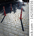 Bright Red Delineators Stand on Cobblestones Under Soft Sunlight 142580556