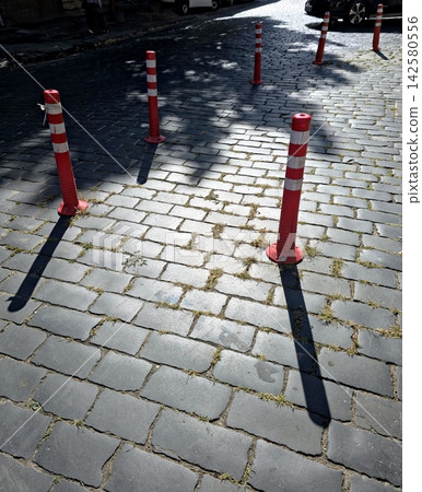 Bright Red Delineators Stand on Cobblestones Under Soft Sunlight 142580556