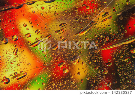 Water Droplets on Colorful Abstract Glass Background. Macro view of water droplets on transparent glass with vivid red, orange, yellow green reflections. Colorful abstract background with condensation 142580587