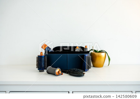 Styling tool attachments spread beside open storage case/ Hair styling tool attachments and barrels spread beside open storage case on dresser, organized beauty equipment for at home hairstyling 142580609
