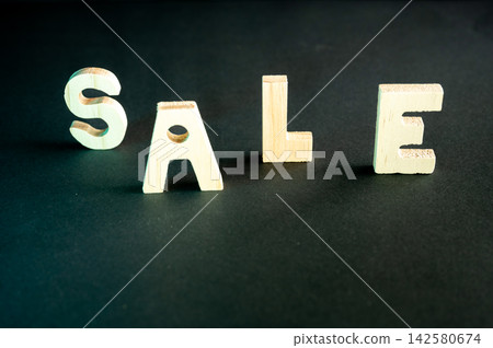 Vivid SALE Sign on a Dark Background. Wooden letters spelling SALE lit with vivid colorful light on a dark background, a creative conceptual image of retail discounts and Black Friday shopping. Vivid SALE Sign on a Dark Background. Wooden letters spelling SALE lit with vivid colorful light on a dark background, a creative conceptual image of retail discounts and Black Friday shopping. 142580674