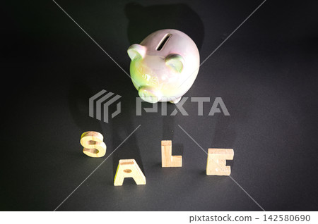 Piggy Bank and the Word SALE. A pink piggy bank beside the word SALE spelled in wooden letters on a dark background, a conceptual image of savings, budgeting and shopping discounts. Piggy Bank and the Word SALE. A pink piggy bank beside the word SALE spelled in wooden letters on a dark background, a conceptual image of savings, budgeting and shopping discounts. 142580690