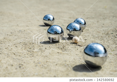 Boules clustered near target jack on sandy park court. Multiple steel boules clustered near small wooden target jack on sandy park court, end of round scoring configuration and game result in outdoor Boules clustered near target jack on sandy park court. Multiple steel boules clustered near small wooden target jack on sandy park court, end of round scoring configuration and game result in outdoor 142580692