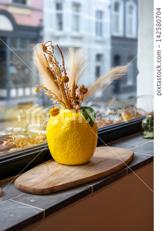 Yellow Vase with Decorative Branches on Window Sill. Bright yellow vase with decorative elements placed on a windowsill, creating a warm and cozy interior atmosphere with natural light. Yellow Vase with Decorative Branches on Window Sill. Bright yellow vase with decorative elements placed on a windowsill, creating a warm and cozy interior atmosphere with natural light. 142580704