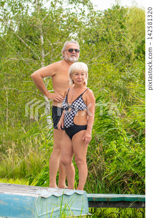 Senior couple standing in swimsuits beside lush outdoor greenery Senior couple standing in swimsuits beside lush outdoor greenery 142581320