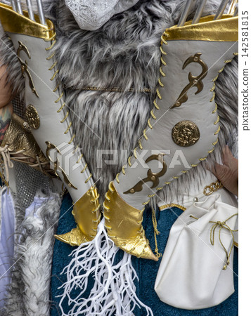 Close up view of a fantasy archers quiver made of grey and gold leather with brass ornaments filled with arrows set against grey fur and teal fabric Close up view of a fantasy archers quiver made of grey and gold leather with brass ornaments filled with arrows set against grey fur and teal fabric 142581815