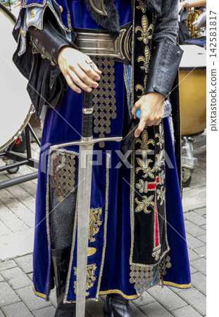 Detailed view of a royal knight costume with sword at a festival event in a busy city square Detailed view of a royal knight costume with sword at a festival event in a busy city square 142581817