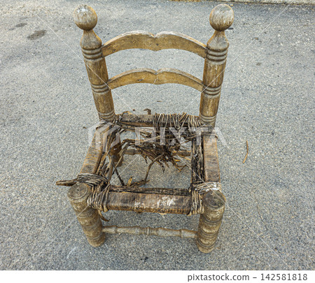 Broken wooden chair with frayed rush seat placed on concrete ground Broken wooden chair with frayed rush seat placed on concrete ground 142581818