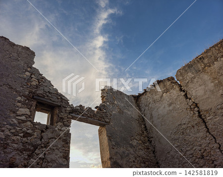 Stone ruin shows open doorways and fractured walls under a blue sky Stone ruin shows open doorways and fractured walls under a blue sky 142581819