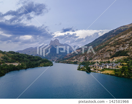 Lanuza Reservoir Winding Through the Tena Valley. Aerial view of the Lanuza reservoir winding through the Tena Valley with a village and distant peaks in the Spanish Pyrenees, Aragon, a peaceful mount Lanuza Reservoir Winding Through the Tena Valley. Aerial view of the Lanuza reservoir winding through the Tena Valley with a village and distant peaks in the Spanish Pyrenees, Aragon, a peaceful mount 142581966