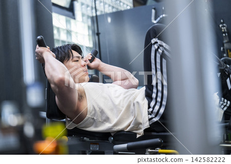 一位年輕男子在健身房進行腿部推舉訓練。 一位年輕男子在健身房進行腿部推舉訓練。 142582222