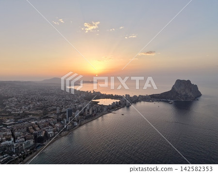 serene sunset over coastal city with beach and rocky outcrop, aerial view from above the cityscape, orange and blue sky, concrete and sand, travel and vacation rentals context. serene sunset over coastal city with beach and rocky outcrop, aerial view from above the cityscape, orange and blue sky, concrete and sand, travel and vacation rentals context. 142582353