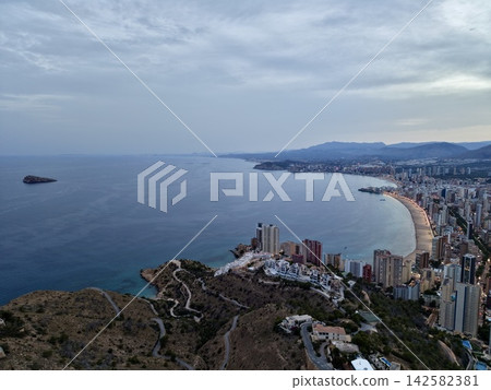 Coastal skyline with crescent beach, calm sea, waterfront towers, and distant rocky island under soft dusk light, with coast, city, skyline, beach detail, showing dusk, sea, island, waterfront context Coastal skyline with crescent beach, calm sea, waterfront towers, and distant rocky island under soft dusk light, with coast, city, skyline, beach detail, showing dusk, sea, island, waterfront context 142582381