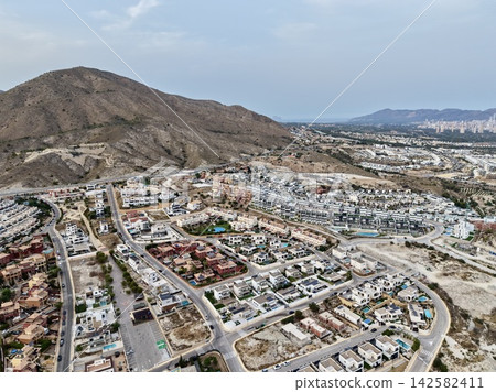 Aerial suburban neighborhood beside dry rugged hill with coastline, city skyline, winding roads, villas, apartments, and wide coastal horizon, with aerial, suburban, neighborhood, residential detail Aerial suburban neighborhood beside dry rugged hill with coastline, city skyline, winding roads, villas, apartments, and wide coastal horizon, with aerial, suburban, neighborhood, residential detail 142582411