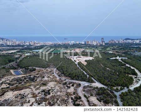 Coastal city skyline with island horizon, wooded hillside foreground, golf course edges, shoreline highrises, calm sea and dusk light over urban bay, with coast, city, skyline, island detail Coastal city skyline with island horizon, wooded hillside foreground, golf course edges, shoreline highrises, calm sea and dusk light over urban bay, with coast, city, skyline, island detail 142582428