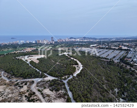 Panoramic coastal skyline with highrise towers above forested hills, shoreline roads, island view, urban waterfront, and soft blue sky at calm evening light, with coast, skyline, highrise, tower Panoramic coastal skyline with highrise towers above forested hills, shoreline roads, island view, urban waterfront, and soft blue sky at calm evening light, with coast, skyline, highrise, tower 142582429