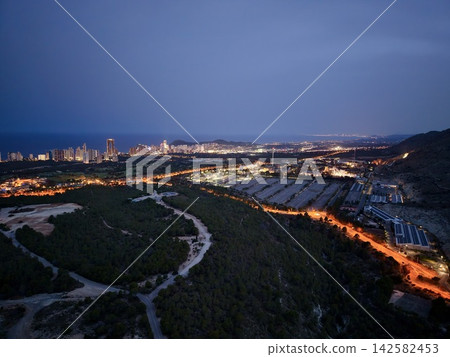 Coastal city skyline glowing at dusk above shoreline roads, dark hillside foreground, harbor lights, and deep blue sky creating panoramic urban seascape, with city, skyline, dusk, twilight detail Coastal city skyline glowing at dusk above shoreline roads, dark hillside foreground, harbor lights, and deep blue sky creating panoramic urban seascape, with city, skyline, dusk, twilight detail 142582453