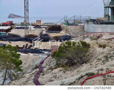 Coastal construction site with stacked rebar, concrete retaining forms, deep excavation, scaffolding, utility pipes and shoreline views beside sea, with construction, coastal, excavation, rebar detail Coastal construction site with stacked rebar, concrete retaining forms, deep excavation, scaffolding, utility pipes and shoreline views beside sea, with construction, coastal, excavation, rebar detail 142582480
