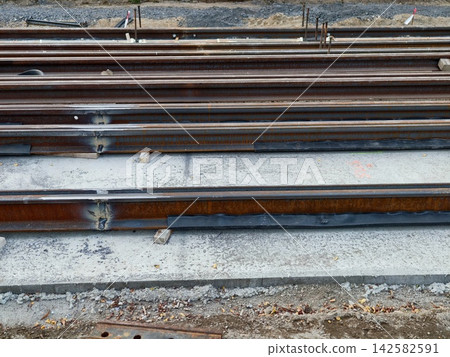 construction site with railroad tracks under development, concrete sleepers and steel materials visible, industrial ground-level perspective, gray and brown tones. construction site with railroad tracks under development, concrete sleepers and steel materials visible, industrial ground-level perspective, gray and brown tones. 142582591
