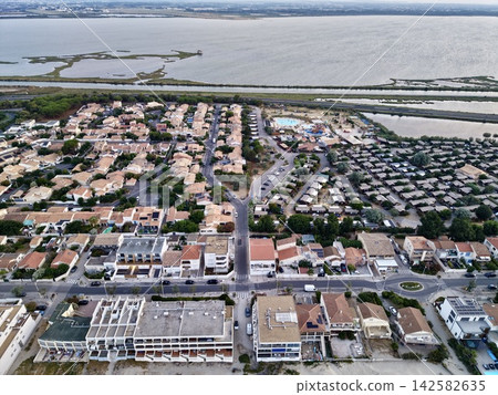 stationary aerial view of relaxed residential area near water in coastal town with concrete, wood, and metal structures and greenery and blue skies, brown and white houses and roads, pools. stationary aerial view of relaxed residential area near water in coastal town with concrete, wood, and metal structures and greenery and blue skies, brown and white houses and roads, pools. 142582635