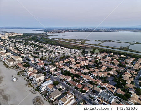 peaceful coastal town with residential buildings and wetlands near a body of water, serene aerial view of tranquil real estate area for vacation rentals and tourism. peaceful coastal town with residential buildings and wetlands near a body of water, serene aerial view of tranquil real estate area for vacation rentals and tourism. 142582636