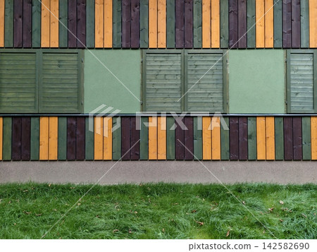 Colorful wooden wall static, in outdoor, with wooden planks, green panels, from a ground-level perspective, with brown, green accents, and neutral mood, with nearby objects. 142582690