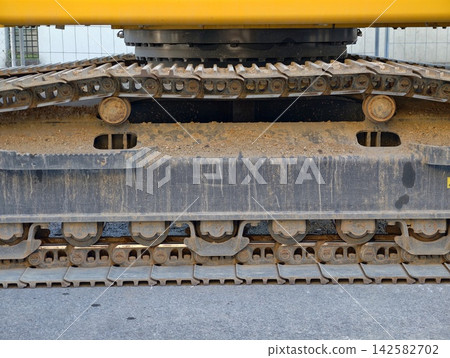 Close up of heavy excavator track system under bright yellow boom at construction site, with excavator, track, system, under detail, showing yellow, boom, construction, site context Close up of heavy excavator track system under bright yellow boom at construction site, with excavator, track, system, under detail, showing yellow, boom, construction, site context 142582702