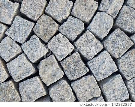 Grey cobblestone pavement composed of tightly arranged square blocks with rough textured surfaces and cool bluish gray stone tones creating durable street pattern Grey cobblestone pavement composed of tightly arranged square blocks with rough textured surfaces and cool bluish gray stone tones creating durable street pattern 142582837
