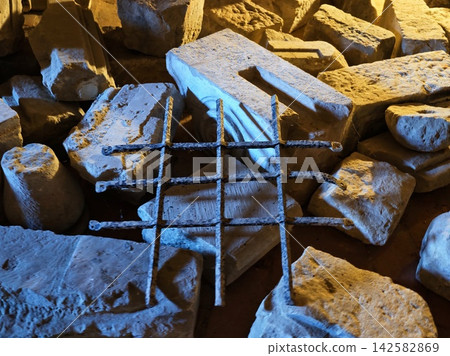 Rough limestone blocks and rusted metal grid piled in quarry, weathered textures, angular edges, crevices, and varied surfaces illuminated by dramatic blue amber lighting across stone Rough limestone blocks and rusted metal grid piled in quarry, weathered textures, angular edges, crevices, and varied surfaces illuminated by dramatic blue amber lighting across stone 142582869