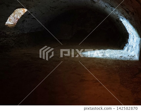 Dark tunnel with rugged stone arch illuminated by daylight at entrance, rough brick opening and shadowed walls, with cave, tunnel, arch, stone detail, showing rock, brick, wall, floor context Dark tunnel with rugged stone arch illuminated by daylight at entrance, rough brick opening and shadowed walls, with cave, tunnel, arch, stone detail, showing rock, brick, wall, floor context 142582870