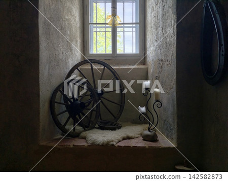 Sunlit window in weathered stone room reveals rustic interior with antique wagonwheel, metal candle holder, soft fur rug, and calm historic ambiance, with window, rustic, interior, antique detail Sunlit window in weathered stone room reveals rustic interior with antique wagonwheel, metal candle holder, soft fur rug, and calm historic ambiance, with window, rustic, interior, antique detail 142582873
