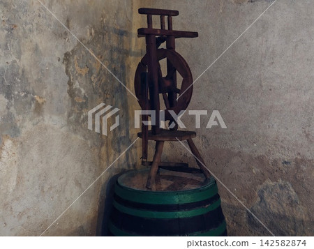 Antique wooden spinning wheel resting against worn textured wall in dim light rustic centerpiece, with antique, wooden, spinning, wheel detail, showing rustic, wall, textured, plaster context Antique wooden spinning wheel resting against worn textured wall in dim light rustic centerpiece, with antique, wooden, spinning, wheel detail, showing rustic, wall, textured, plaster context 142582874