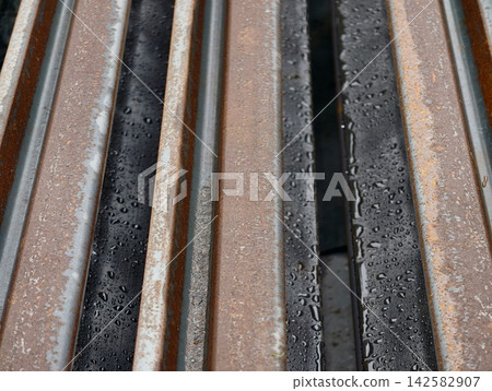 Close-up view of weathered rusted metal rails with water droplets on damp surfaces between aged iron bars, emphasizing texture and industrial detail, with rust, rusted, metal, rail detail 142582907