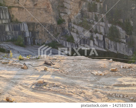 Quarry rockface with layered sedimentary cliffs, dusty ground, scattered rubble, openpit excavation visible under rugged natural light, with quarry, rock, cliff, cliffside detail Quarry rockface with layered sedimentary cliffs, dusty ground, scattered rubble, openpit excavation visible under rugged natural light, with quarry, rock, cliff, cliffside detail 142583133