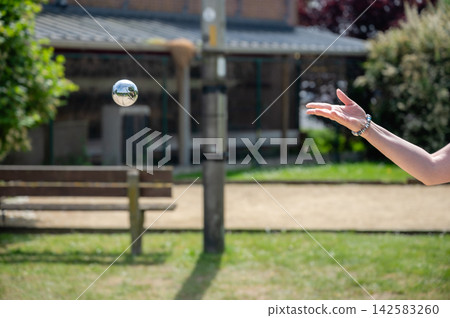 Woman holding two petanque balls ready for next throw. Woman standing on court holding steel petanque ball with second ball ready in other hand, prepared outdoor game moment between throws in sun Woman holding two petanque balls ready for next throw. Woman standing on court holding steel petanque ball with second ball ready in other hand, prepared outdoor game moment between throws in sun 142583260
