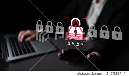 Business professional using laptop and smartphone with data breach alert illustration on a dark background emphasizing cybersecurity issues and privacy concerns Ledger 142583641