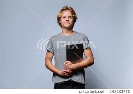 Portrait of confident teenage student holding closed laptop Portrait of confident teenage student holding closed laptop 142583778