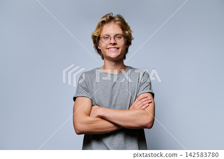 Smiling male student wearing eyeglasses standing with crossed arms on grey background Smiling male student wearing eyeglasses standing with crossed arms on grey background 142583780