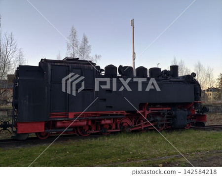 Quiet old train. Historic steam engine sits silently amidst peaceful museum landscape during evening Quiet old train. Historic steam engine sits silently amidst peaceful museum landscape during evening 142584218