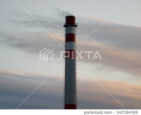 Silhouetted industrial chimney against evening sky emphasizing structural and energy themes Silhouetted industrial chimney against evening sky emphasizing structural and energy themes 142584388