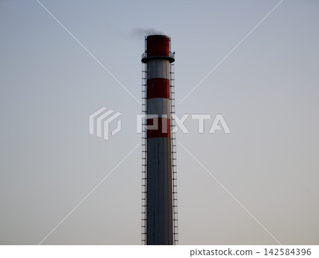 Isolation of industrial tower. Stark profile of lone chimney against muted sky highlights separation 142584396