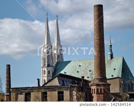 Ancient cathedral features and modern industrial structures coexist beneath bright azure sky Ancient cathedral features and modern industrial structures coexist beneath bright azure sky 142584514