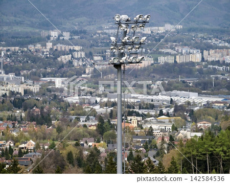 Lighting infrastructure monument casting glow over city and surrounding mountainous terrain with factories Lighting infrastructure monument casting glow over city and surrounding mountainous terrain with factories 142584536